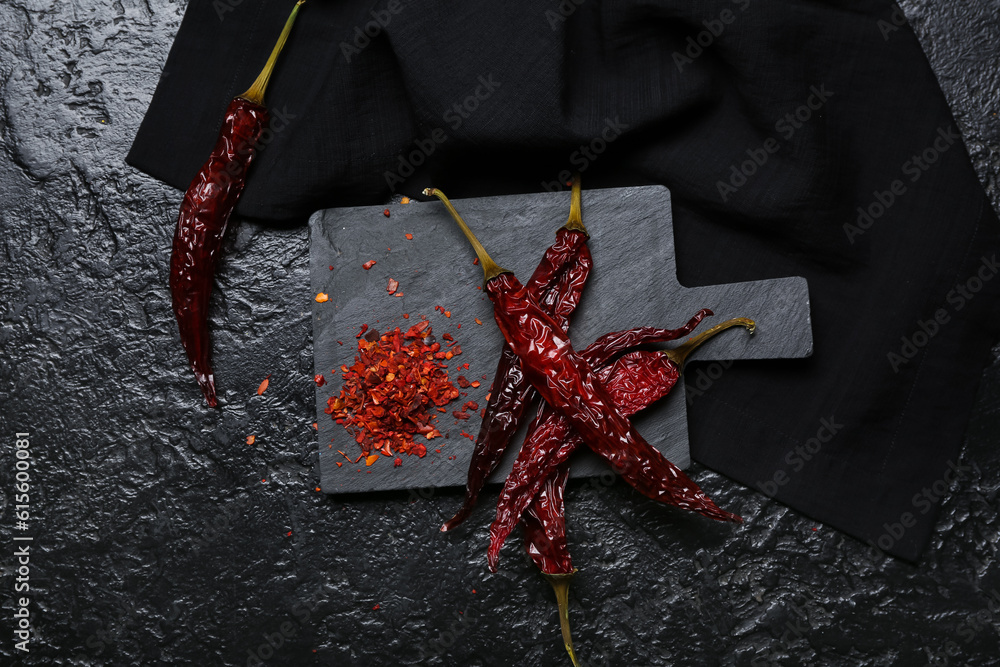 Board with dry chili and ground peppers on dark background