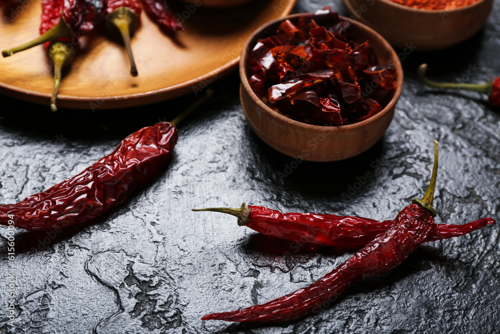 Plate with dry chili peppers and bowls of spices on dark background