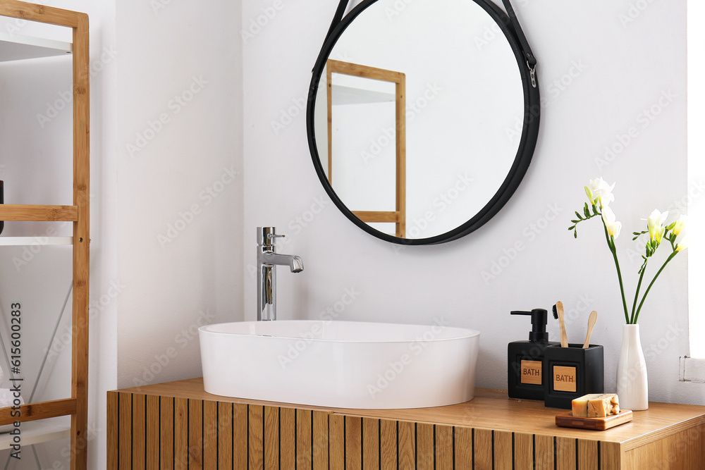 White sink, bath accessories and vase with flowers on table in room