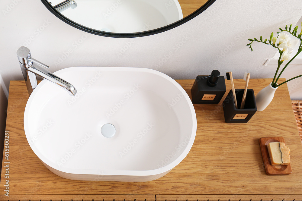 White sink, bath accessories and vase with flowers on table in room