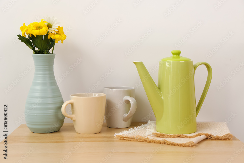 Teapot with cups and flowers on wooden table