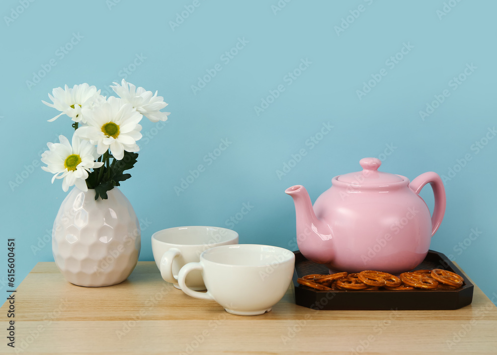 Tea set with tasty pretzels and flowers on wooden table