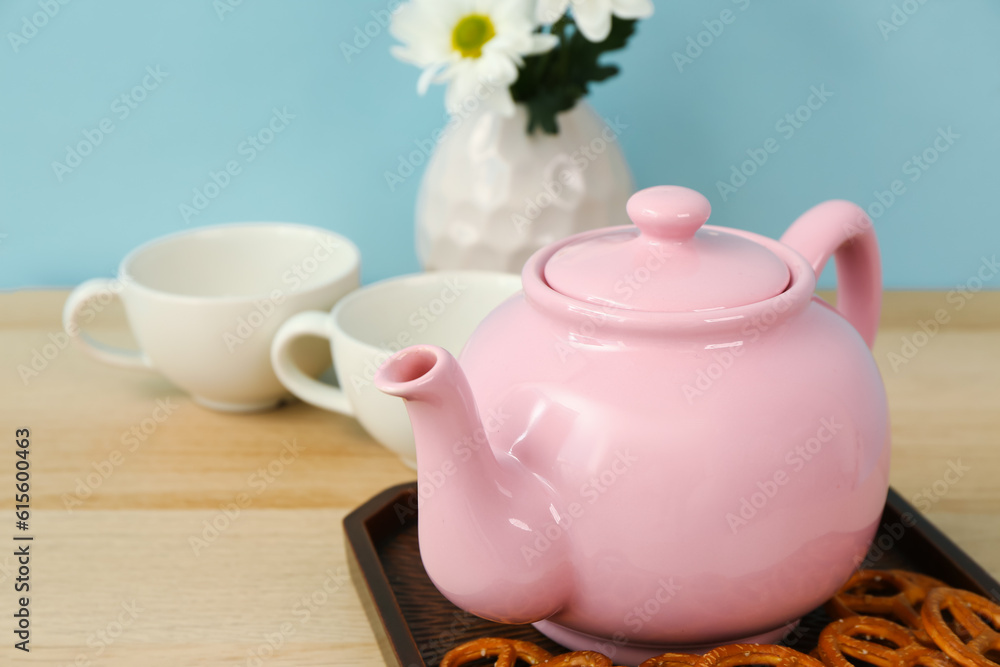 Tea set with tasty pretzels and flowers on wooden table