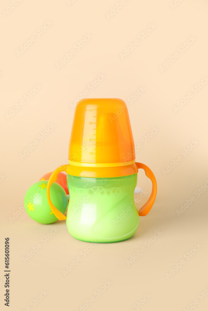 Bottle of milk for baby with rattle on pale orange background