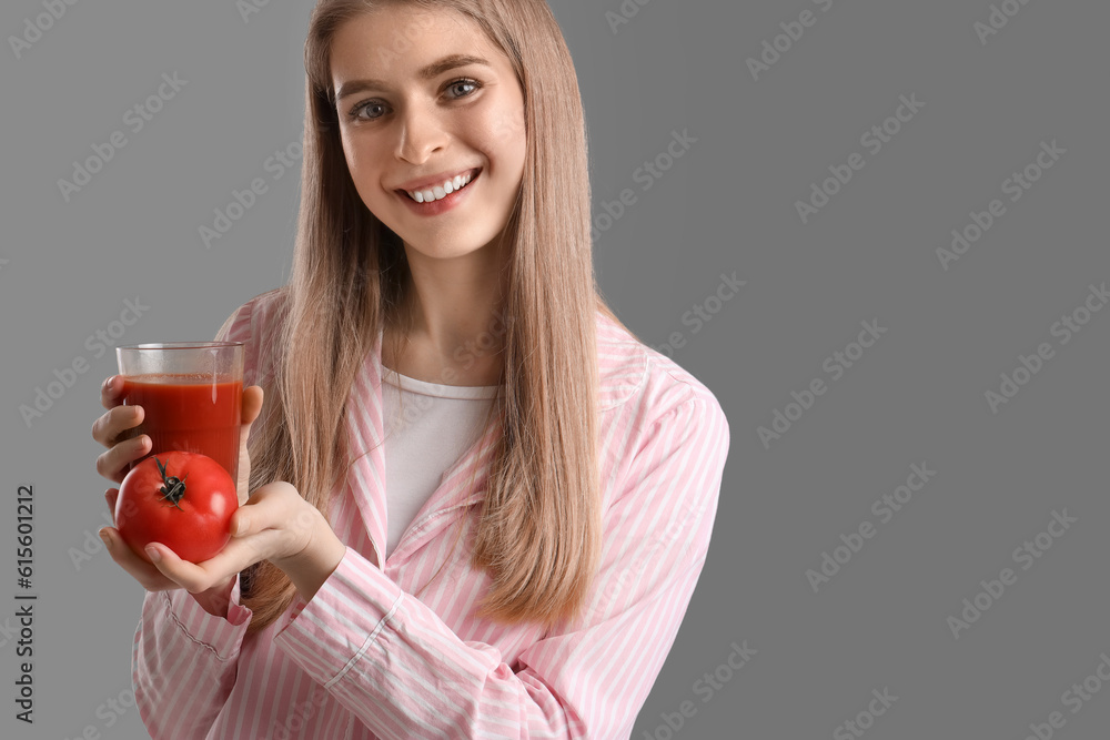 Young woman with glass of vegetable juice and tomato on grey background