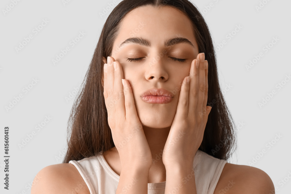 Young woman doing face building exercise on light background, closeup