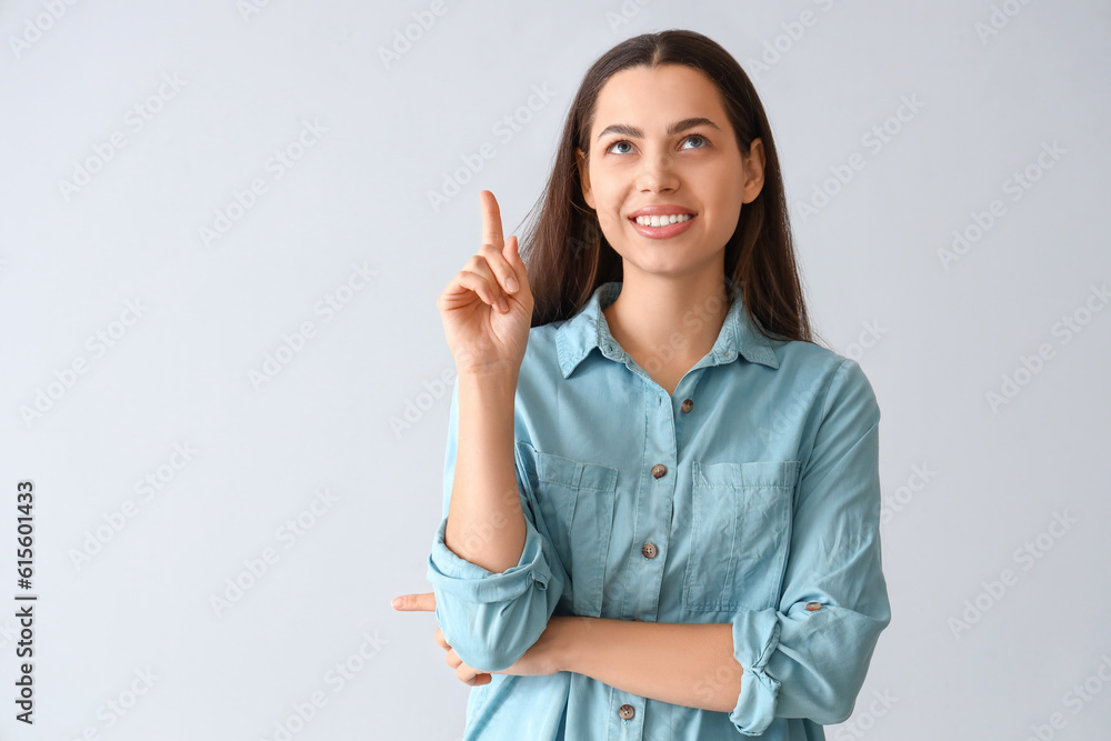 Thoughtful young woman pointing at something on light background