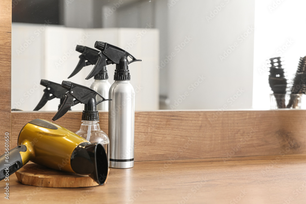 Hairdryer and bottles of spray on table in beauty salon