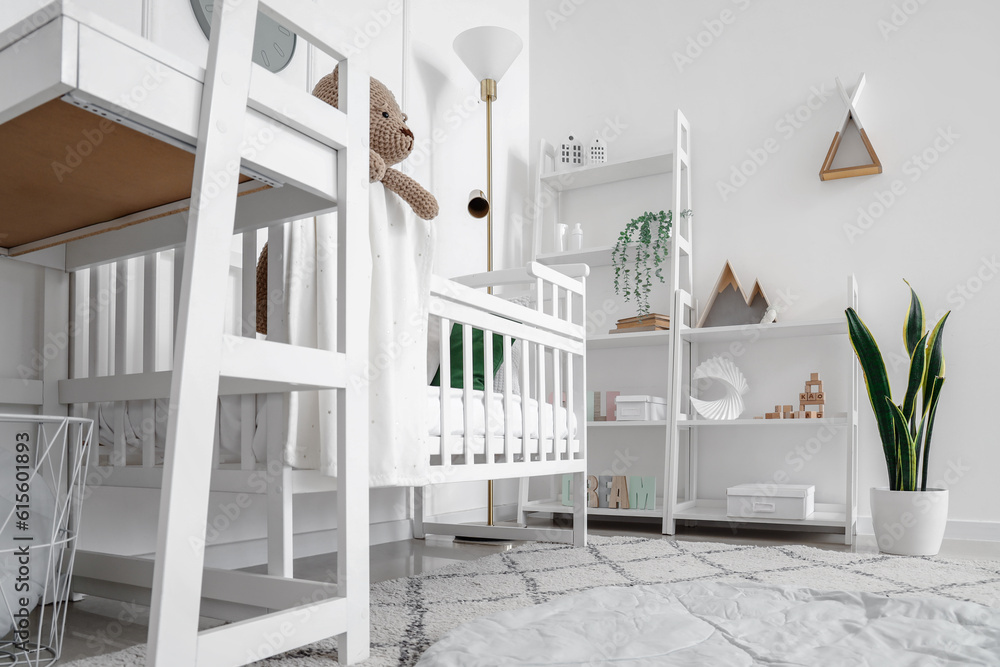 Interior of light bedroom with baby crib, changing table and shelving unit