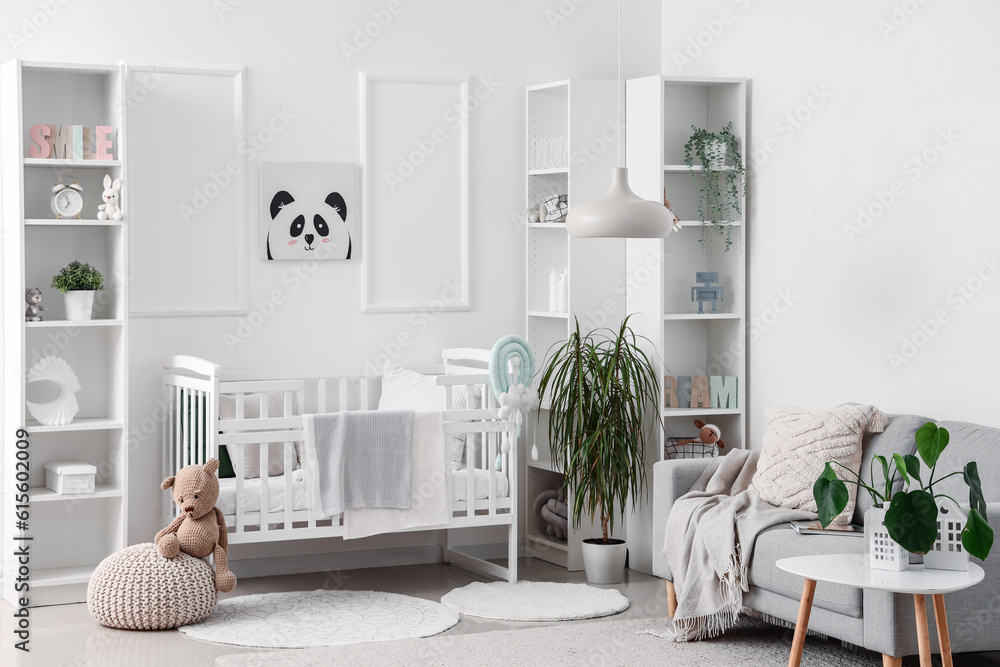 Stylish interior of childrens room in white tones with baby bed and shelving unit