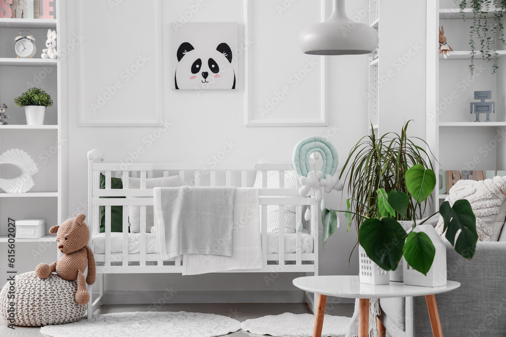 Stylish interior of childrens room in white tones with baby bed and shelving unit