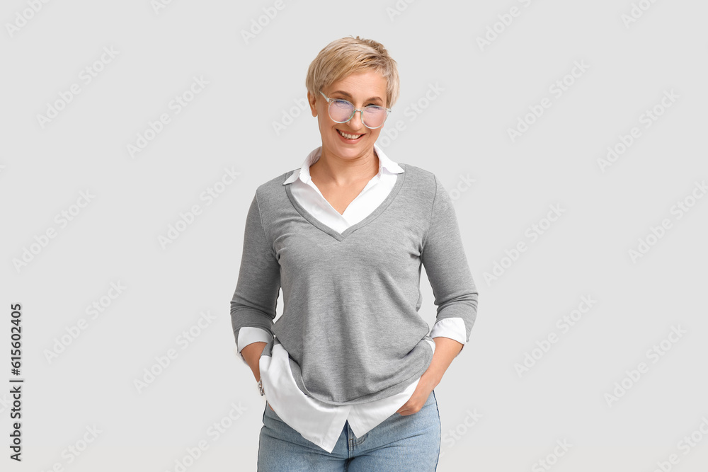 Mature blonde woman in eyeglasses on light background