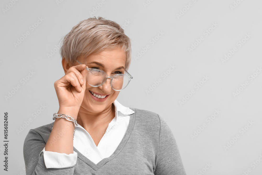 Mature blonde woman in eyeglasses on light background, closeup