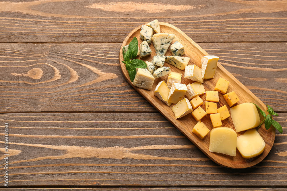 Board with pieces of tasty cheese on wooden background