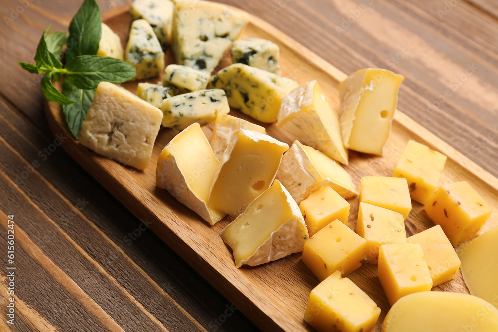 Board with pieces of tasty cheese on wooden background, closeup