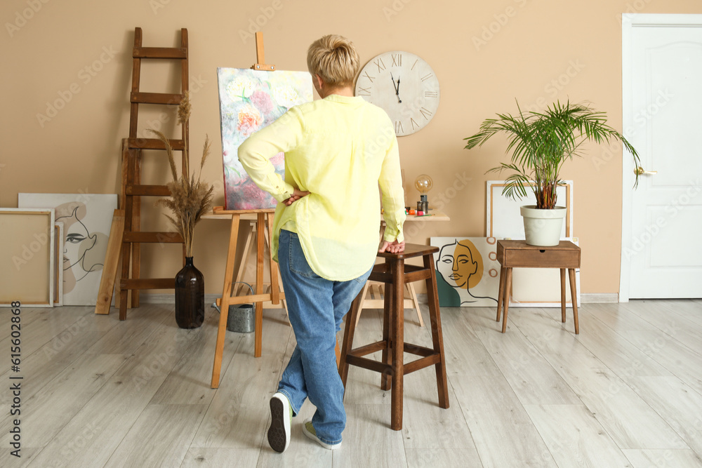 Mature female artist near canvas in  workshop