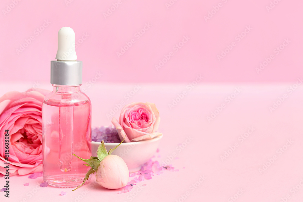 Bottle of cosmetic oil with rose extract and flowers on pink background