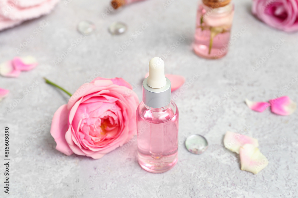 Bottles of cosmetic oil with rose extract and flowers on white table