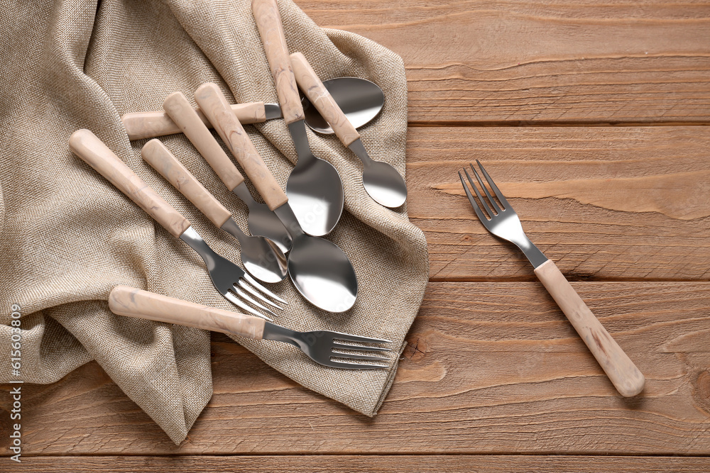 Stainless steel forks and spoons with plastic handles on wooden background