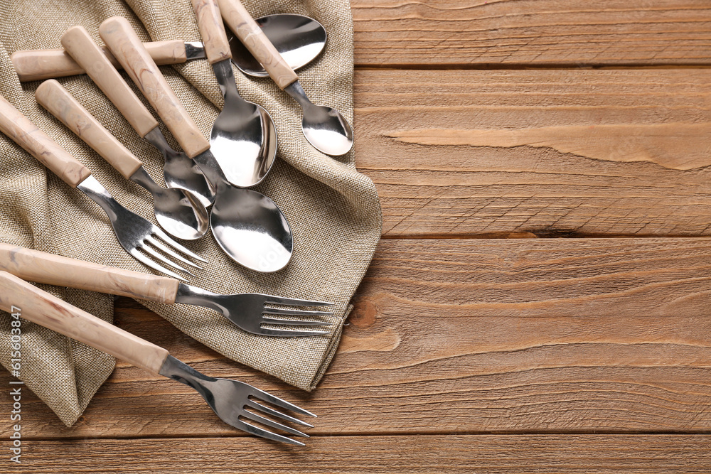 Stainless steel forks and spoons with plastic handles on wooden background