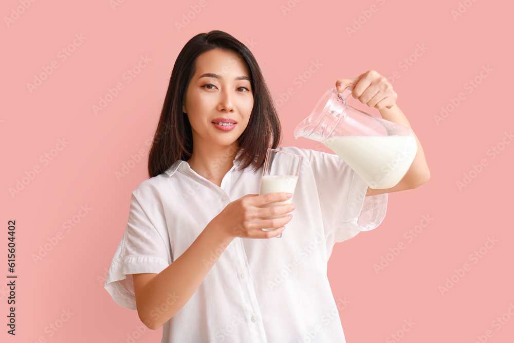 Beautiful Asian woman pouring milk into glass on pink background