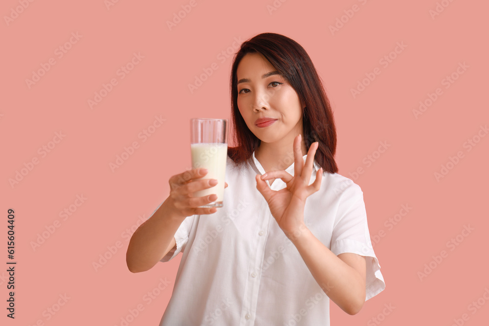 Beautiful Asian woman with glass of milk showing OK on pink background