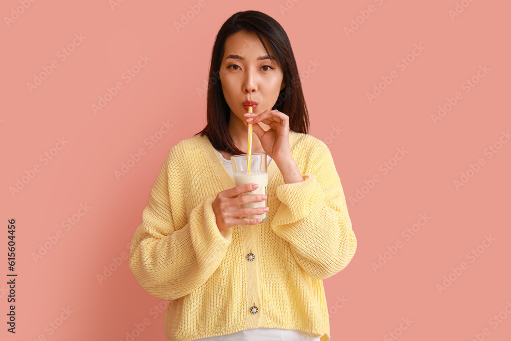 Beautiful Asian woman with glass of milk on pink background