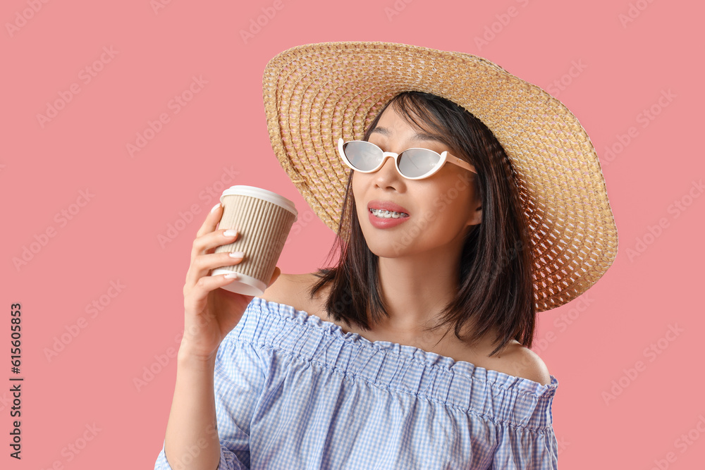 Beautiful Asian woman in stylish sunglasses with cup of coffee on pink background