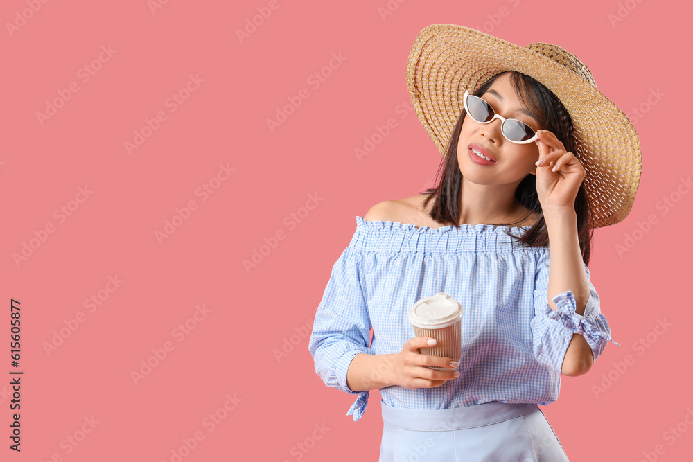 Beautiful Asian woman in stylish sunglasses with cup of coffee on pink background