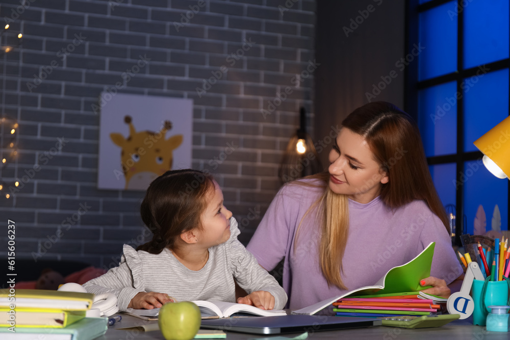 Little girl with her mother doing lessons at home late in evening