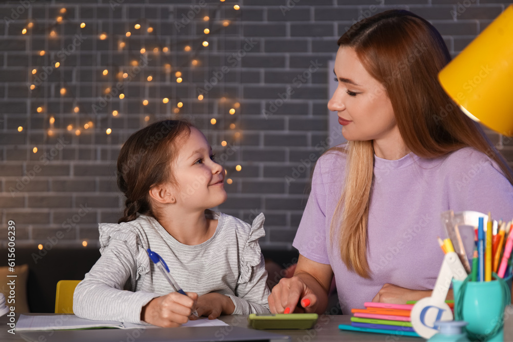 Little girl with her mother doing lessons at home late in evening