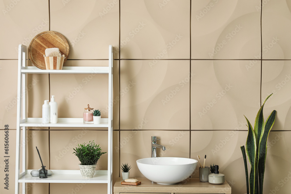 Interior of bathroom with sink bowl, wooden cabinet and shelving unit near beige wall