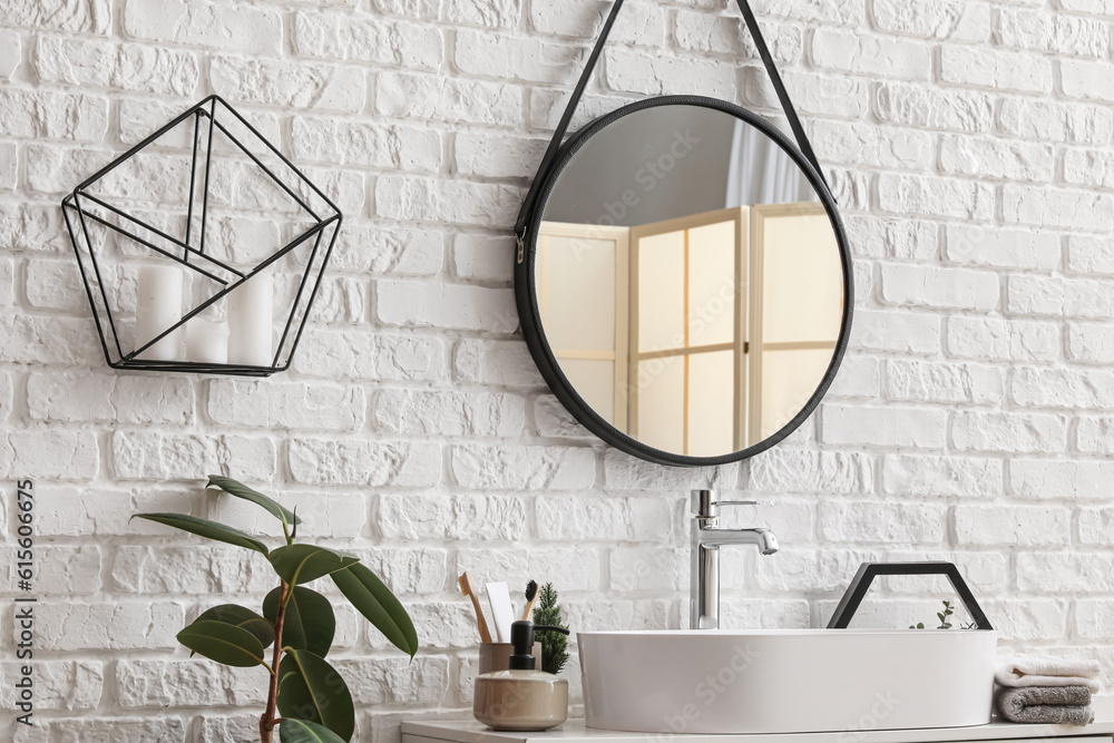 Sink bowl, mirror and bath accessories on table near white brick wall