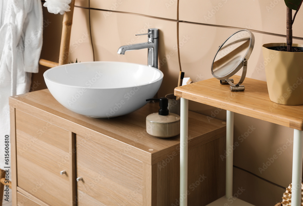 Sink bowl and bath accessories on wooden cabinet in bathroom