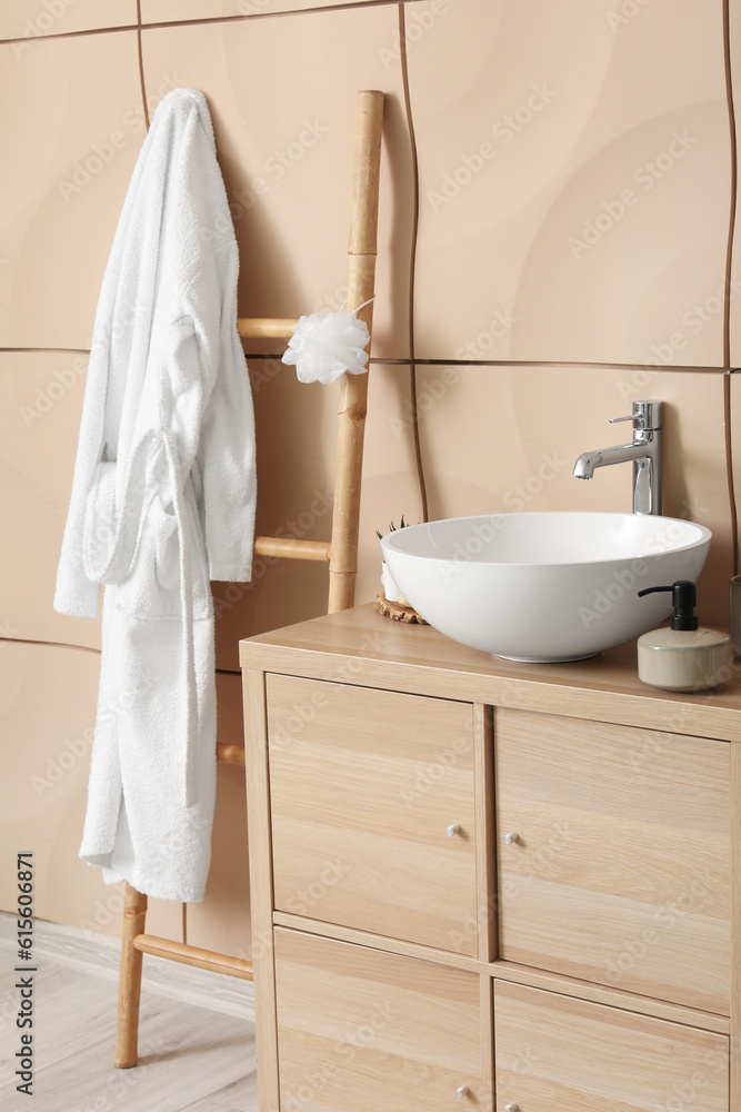 Interior of bathroom with bathrobe, sink bowl and bath accessories on wooden cabinet