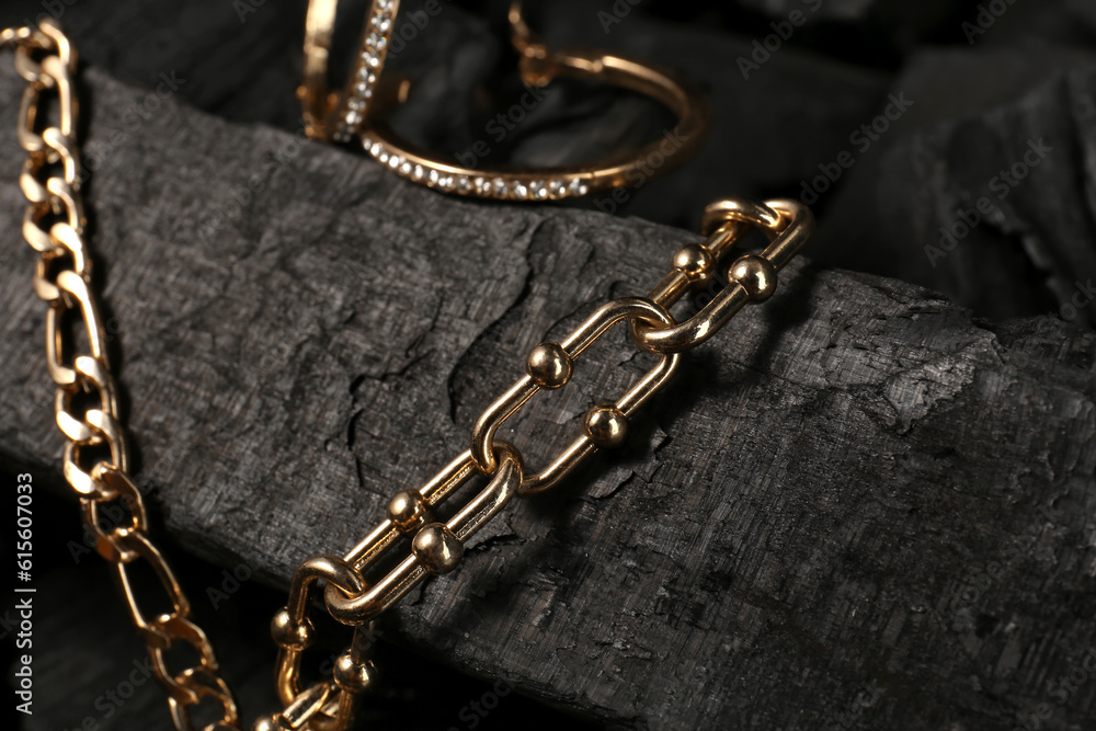 Beautiful chain bracelets and earrings on black charcoal, closeup