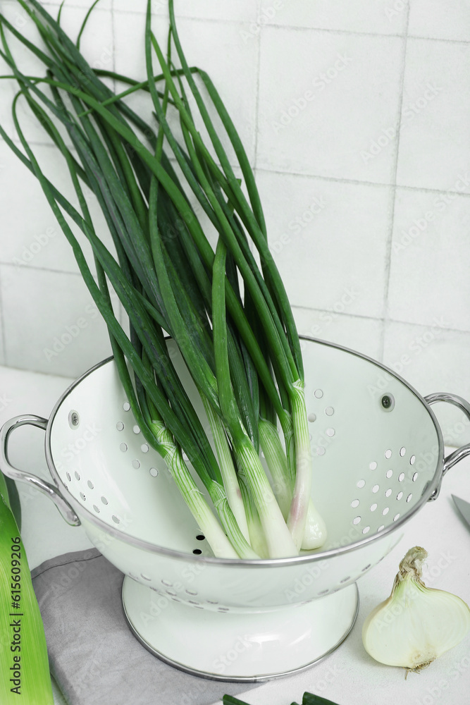 Colander with green onion on light background, closeup