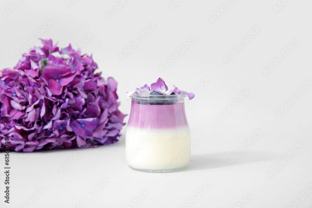 Glass of panna cotta with blueberry and beautiful hydrangea flowers on lilac background