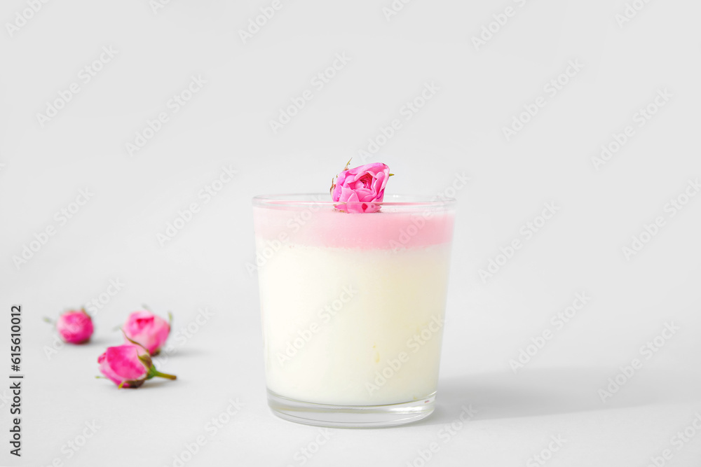 Glass of panna cotta with beautiful pink rose flowers on lilac background