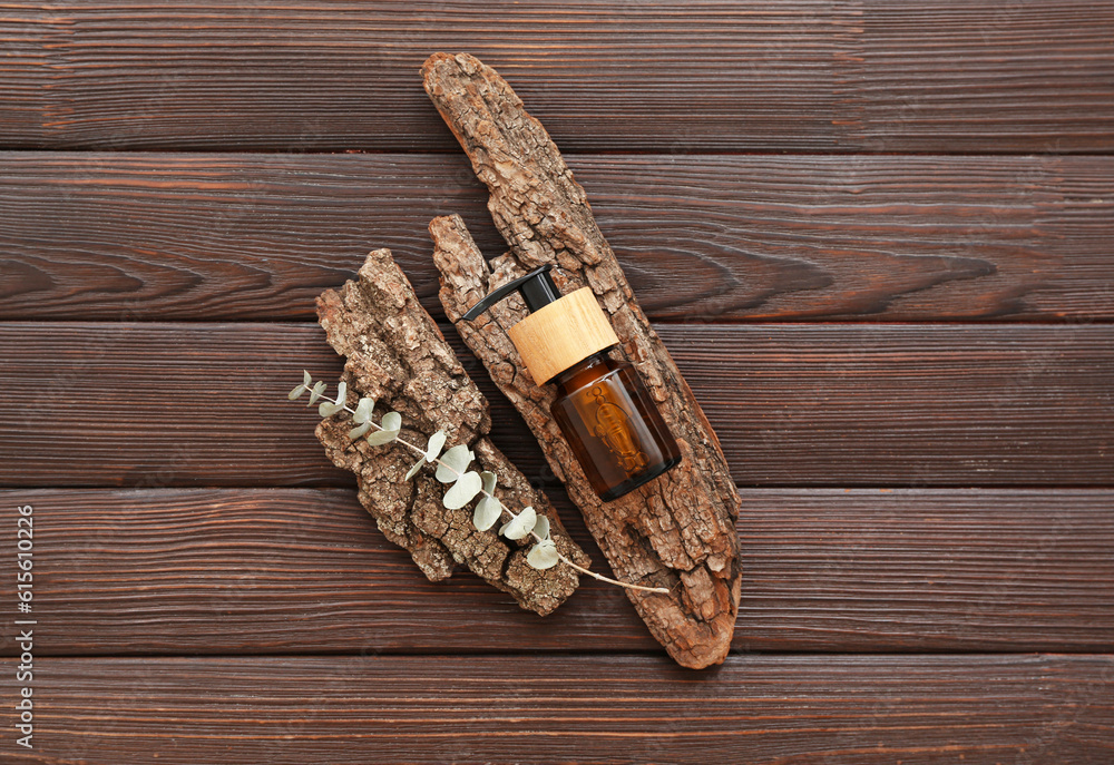 Bottle of cosmetic oil with eucalyptus twig and tree bark on brown wooden background