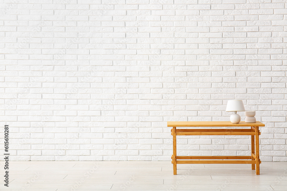 Wooden table with lamp and decorative figure near white brick wall