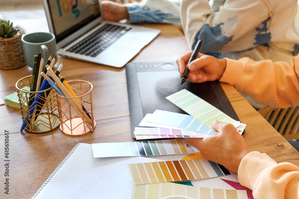 Male graphic designer working with tablet and color palettes at table in office, closeup