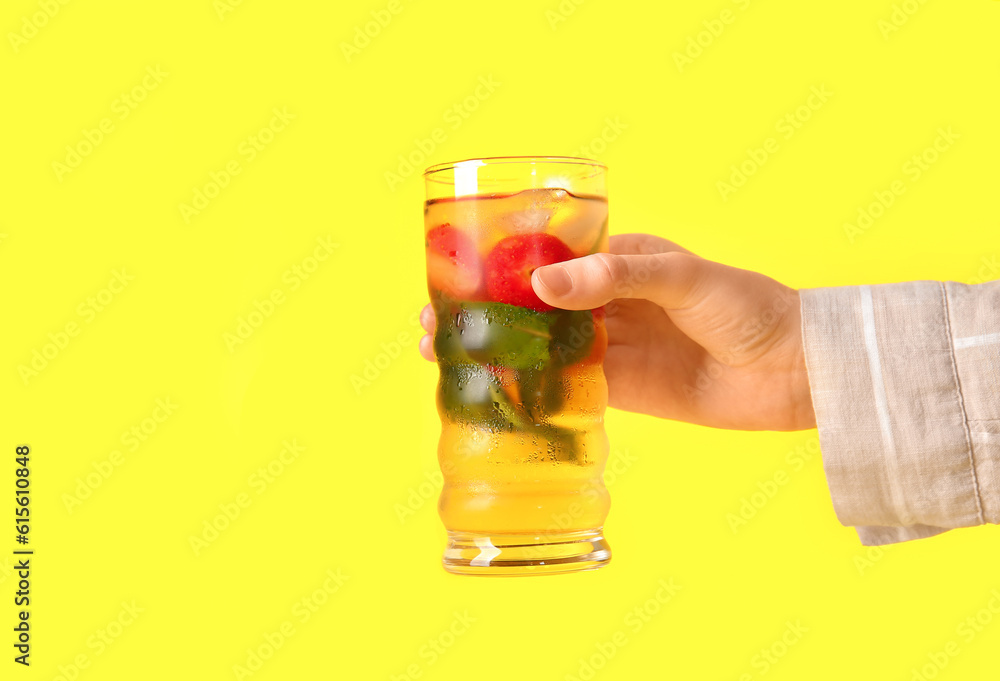 Female hand holding glass of ice tea with strawberry and mint on yellow background