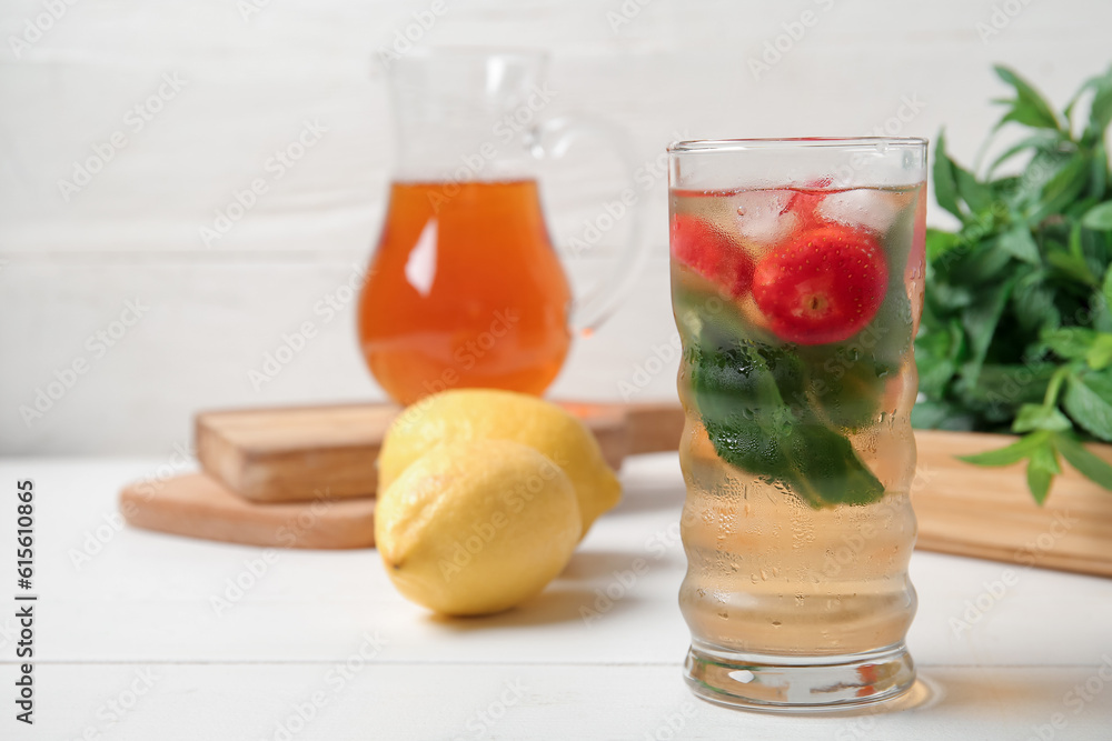 Glass and jug of ice tea with strawberry on white background