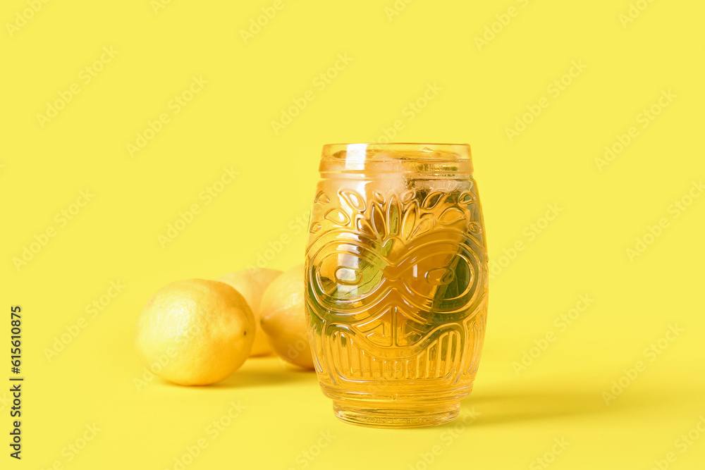 Glass of ice tea with lemon and mint on yellow background