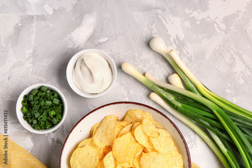 Bowls of tasty sour cream with sliced green onion and potato chips on grey background