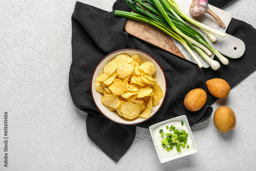 Bowl of tasty sour cream with sliced green onion and potato chips on white background