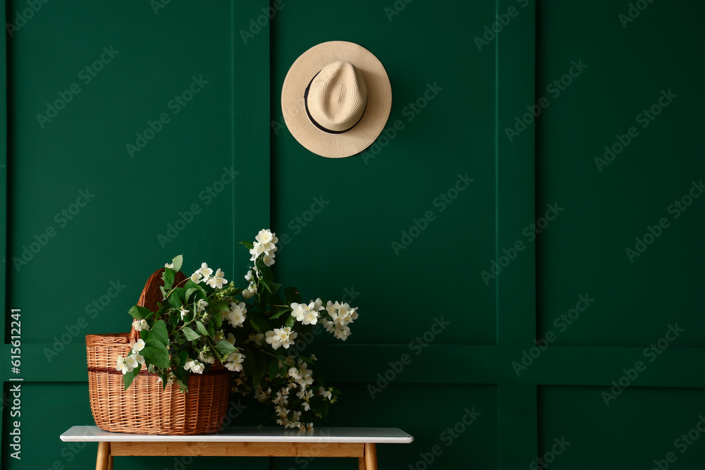 Wicker basket with blooming jasmine flowers on console table near green wall