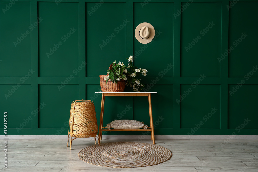 Wicker basket with blooming jasmine flowers on console table near green wall