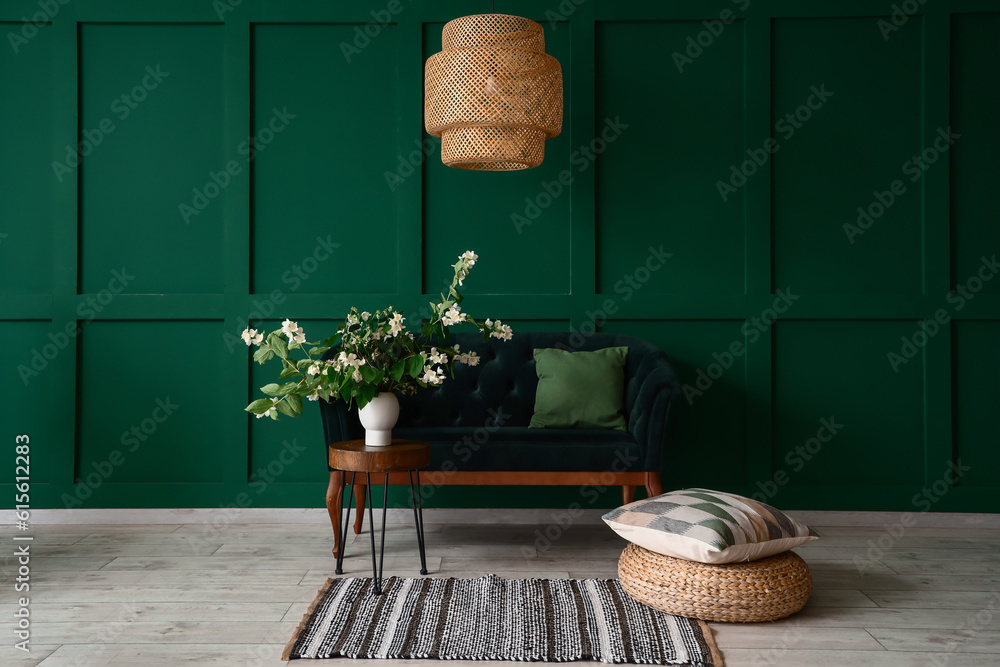 Vase with blooming jasmine flowers on coffee table and sofa near green wall